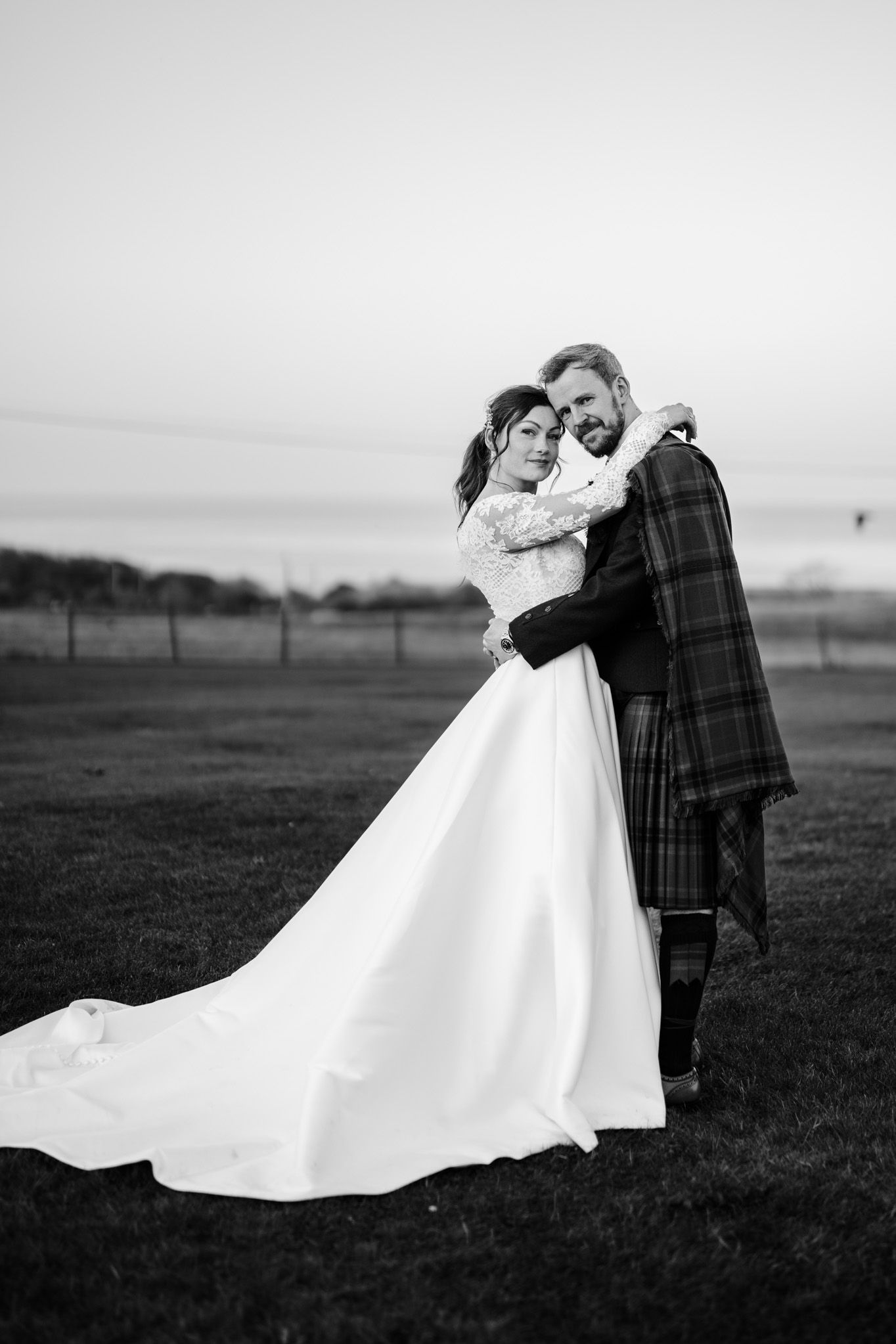 Black and white portrait of newlyweds embracing in an open field.