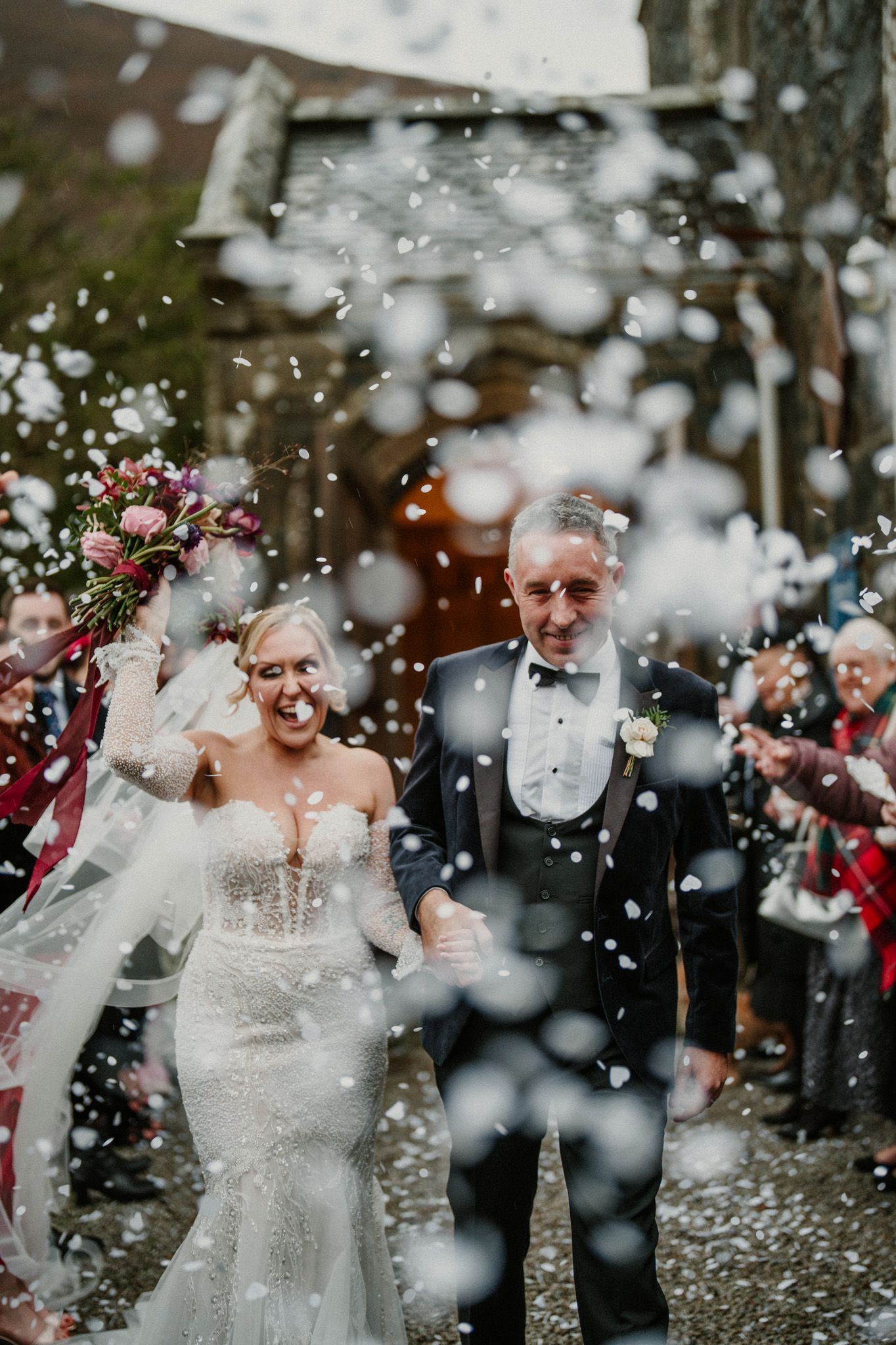 A joyful wedding couple walks through a shower of confetti surrounded by guests on their special day.