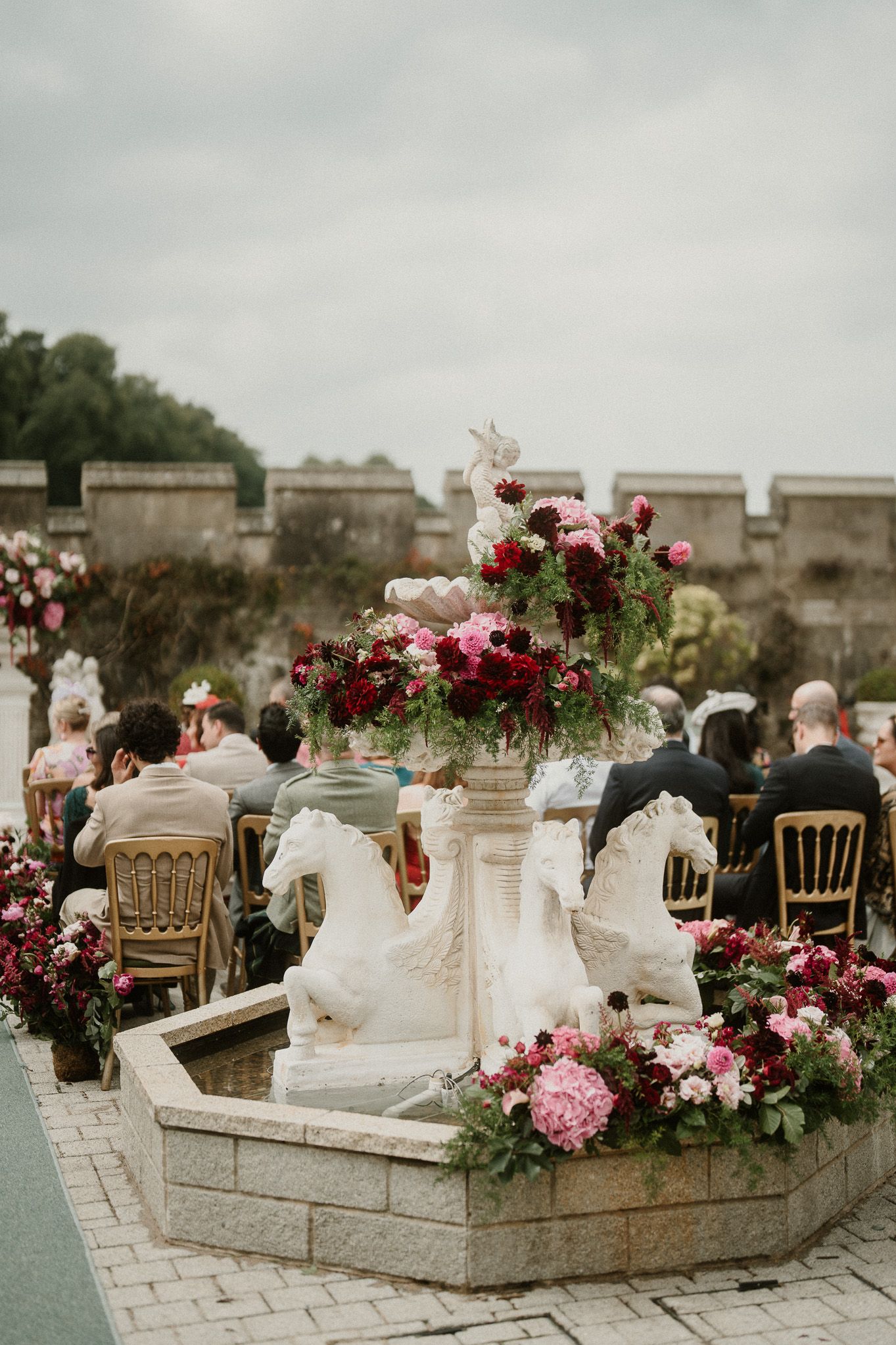 Outdoor wedding reception setup with pink and burgundy floral centerpieces on stone tables.