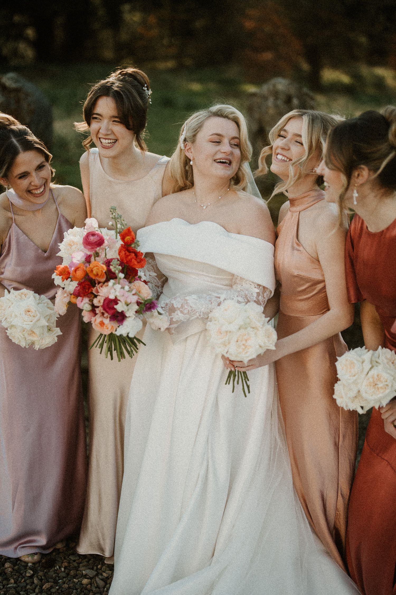Candid moment of bridal party laughing together while holding bouquets in complementary fall colors.
