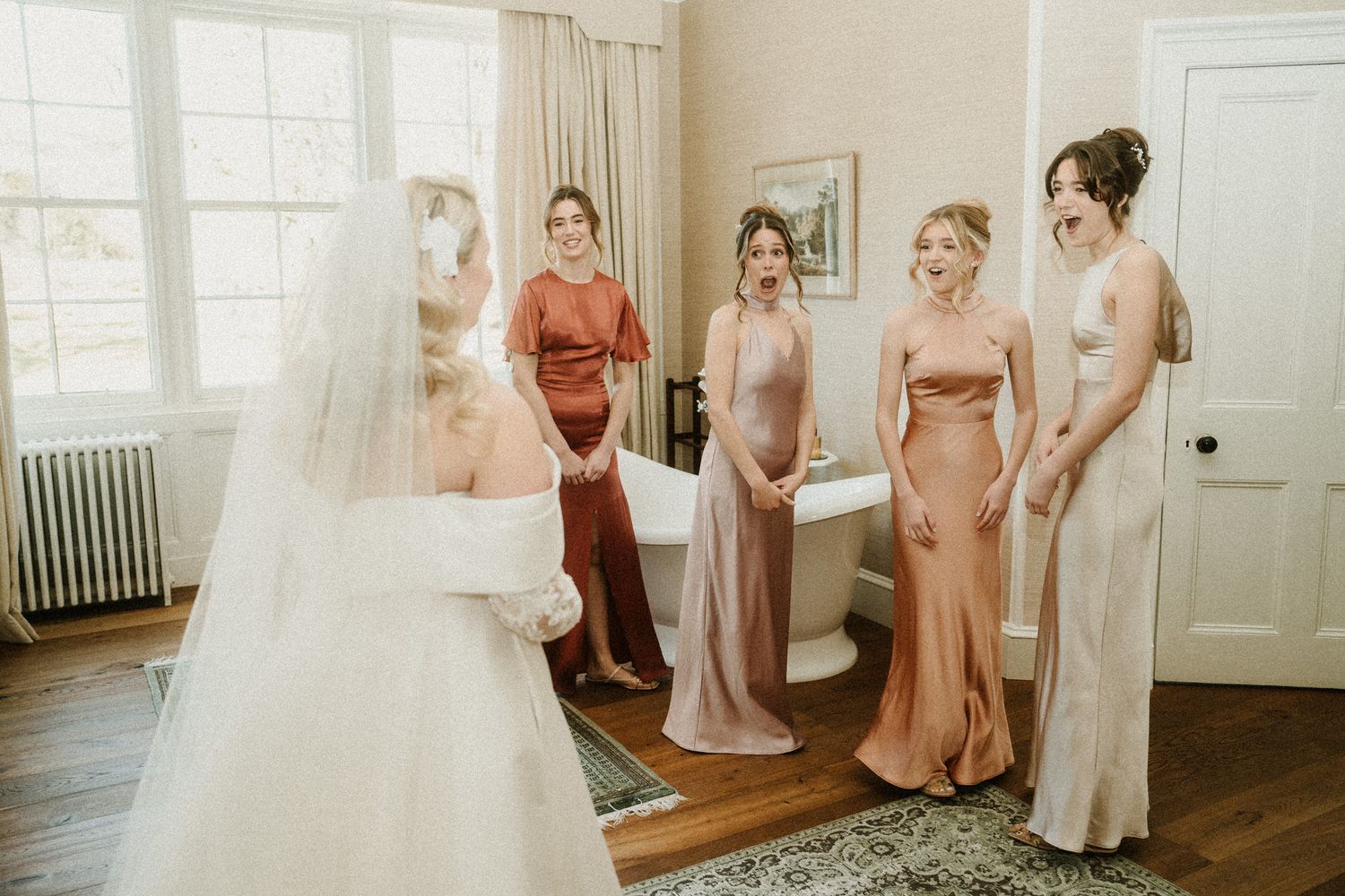 Bridesmaids in blush pink dresses gather around a bride in a traditional white gown.