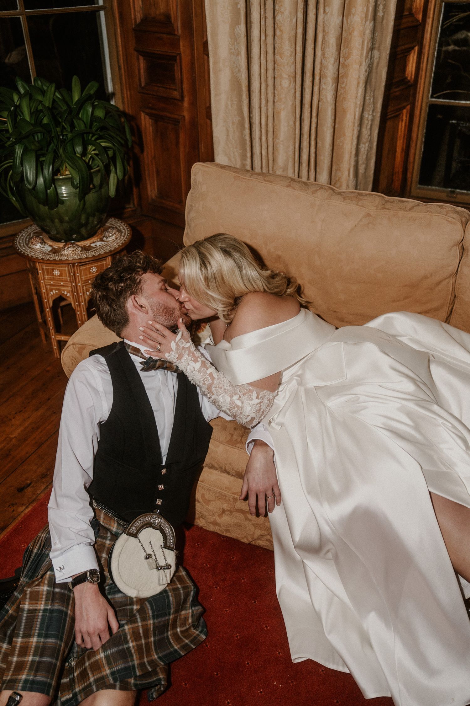 Intimate wedding photos showing a couple lounging on a beige couch in formal attire.