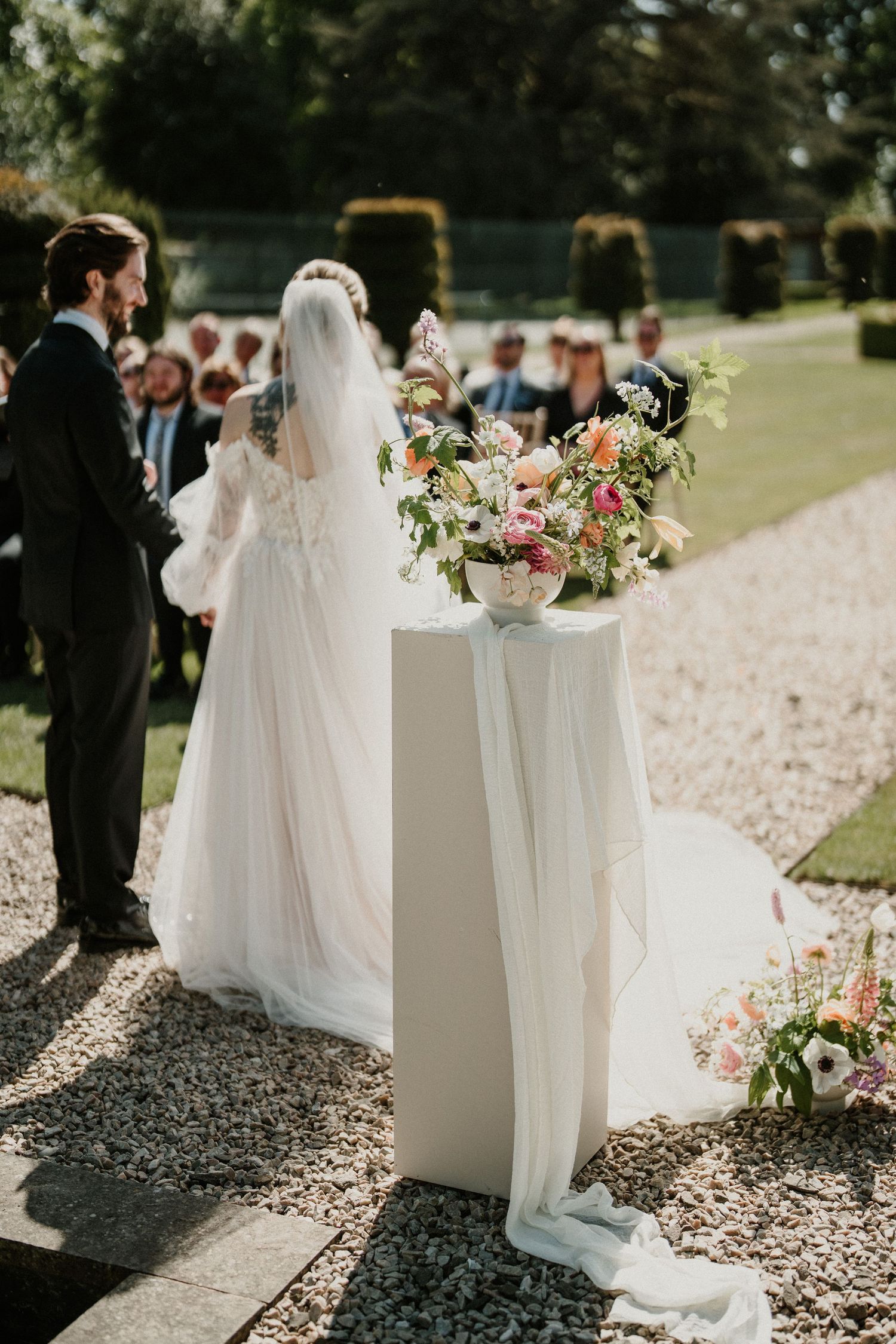 White wedding ceremony decor with floral arrangements on pedestals along a stone pathway.