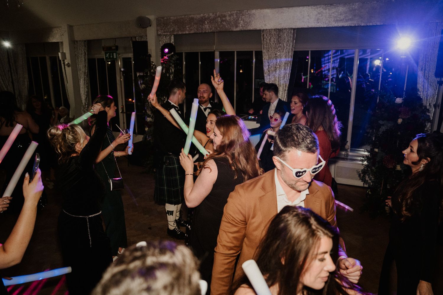 Lively dance floor scene with colorful lighting and raised hands at a wedding reception.