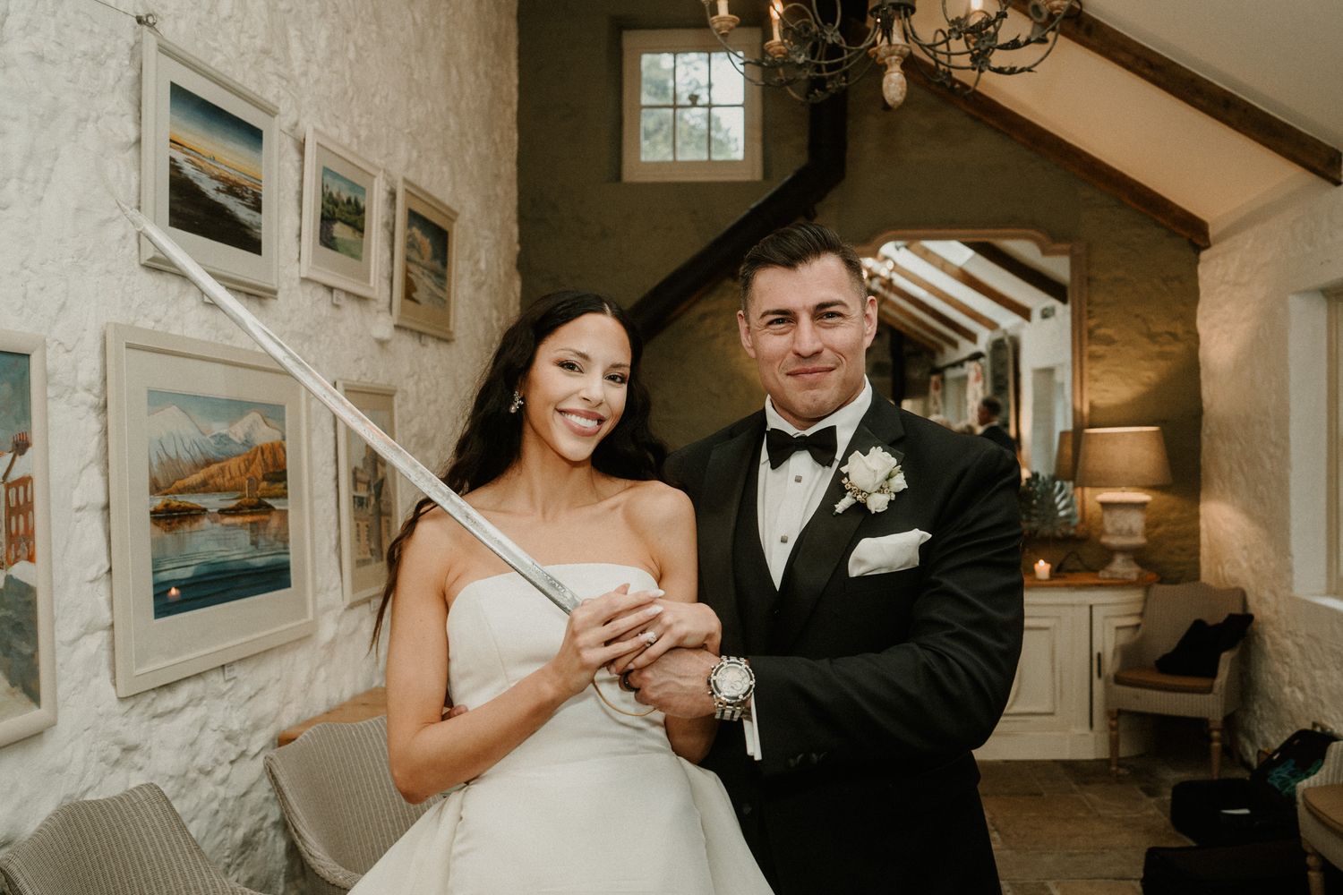 Newlyweds pose together in an elegant indoor setting with framed artwork on the wall.