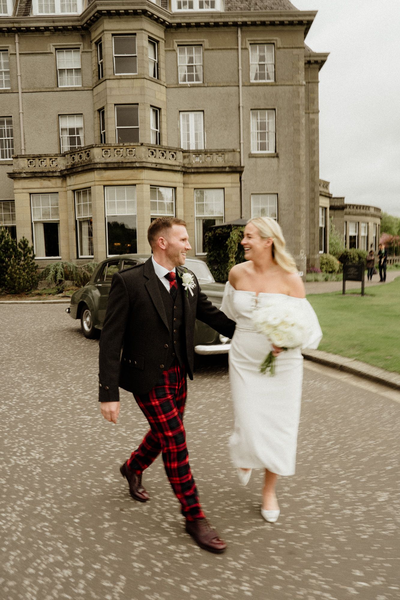 Playful wedding couple dancing outside historic stone mansion.