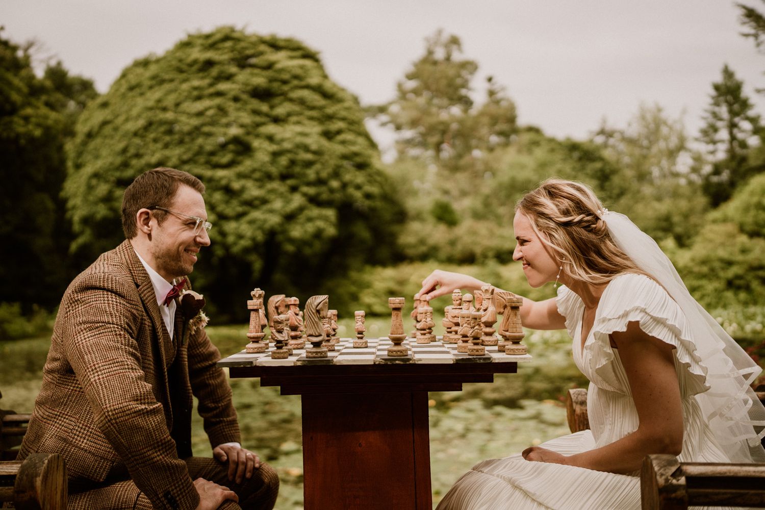 Wedding celebration at a rustic outdoor table set with chess pieces and natural decor.