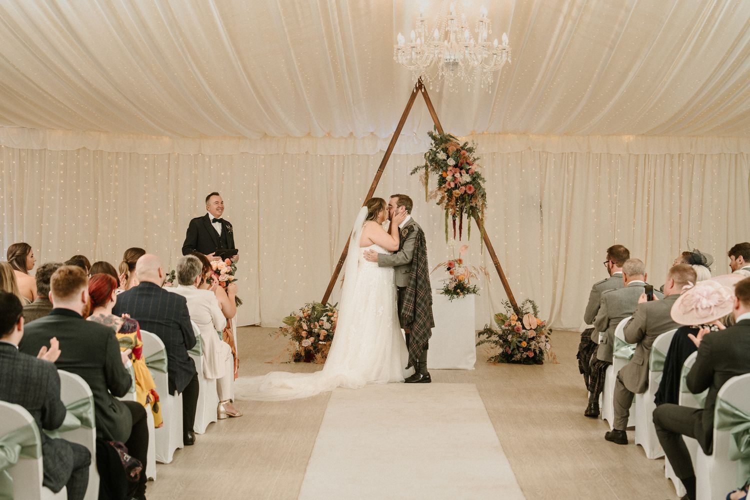 Wedding venue interior with white fabric draped ceiling and wooden arch for ceremony.