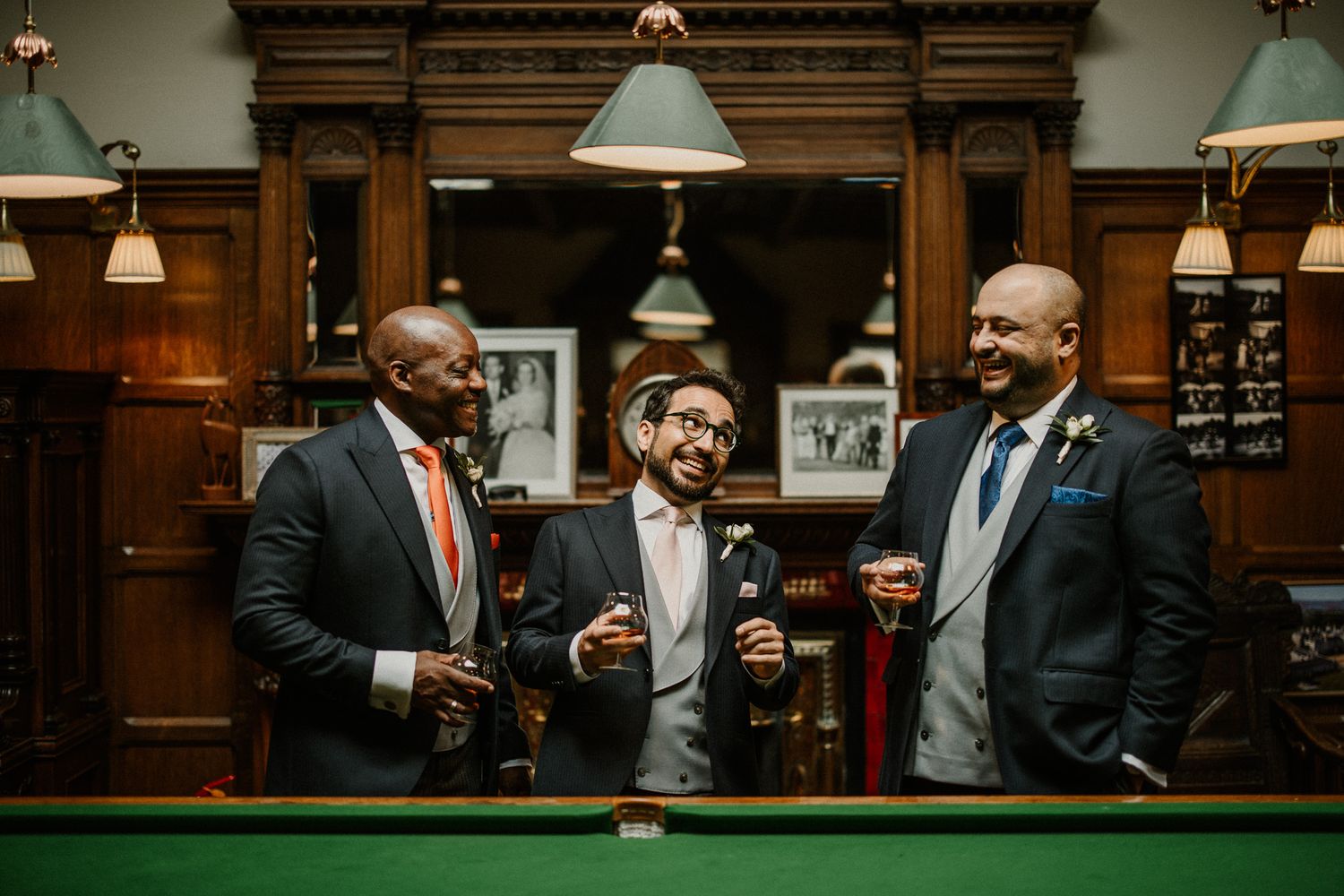 Groomsmen in dark suits gather at a wooden bar for pre-wedding drinks.