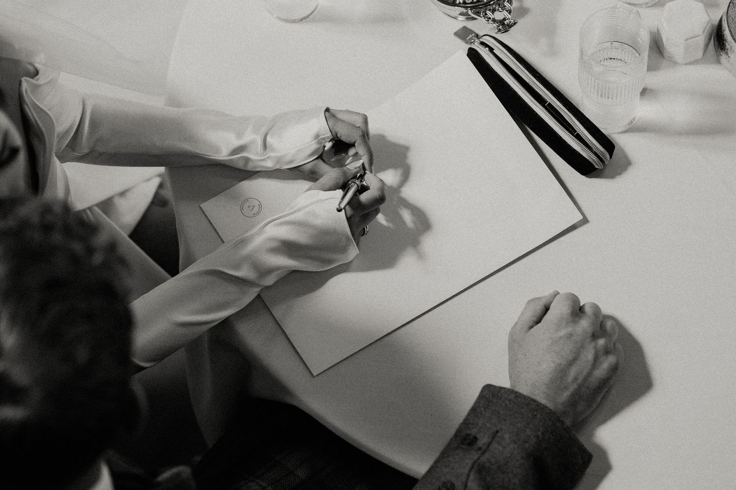 Close-up black and white shots of wedding documents being signed at a ceremony.