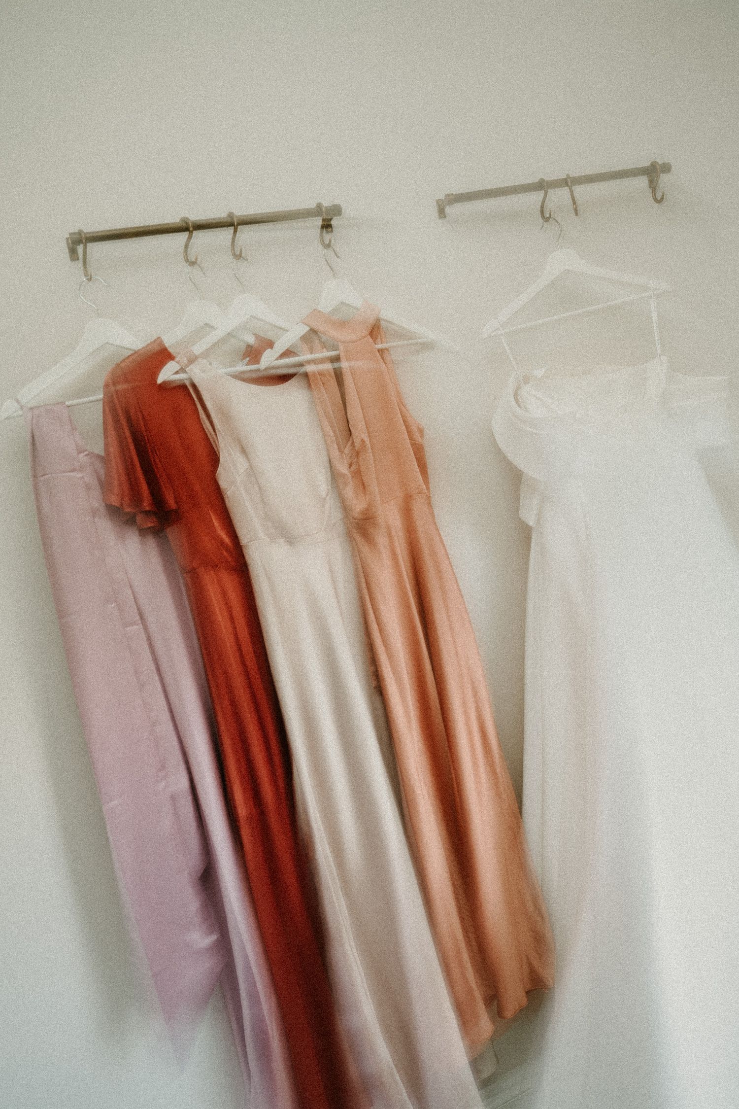 Wedding dresses and bridesmaid gowns in shades of white, coral, and pink hanging on wall-mounted racks.