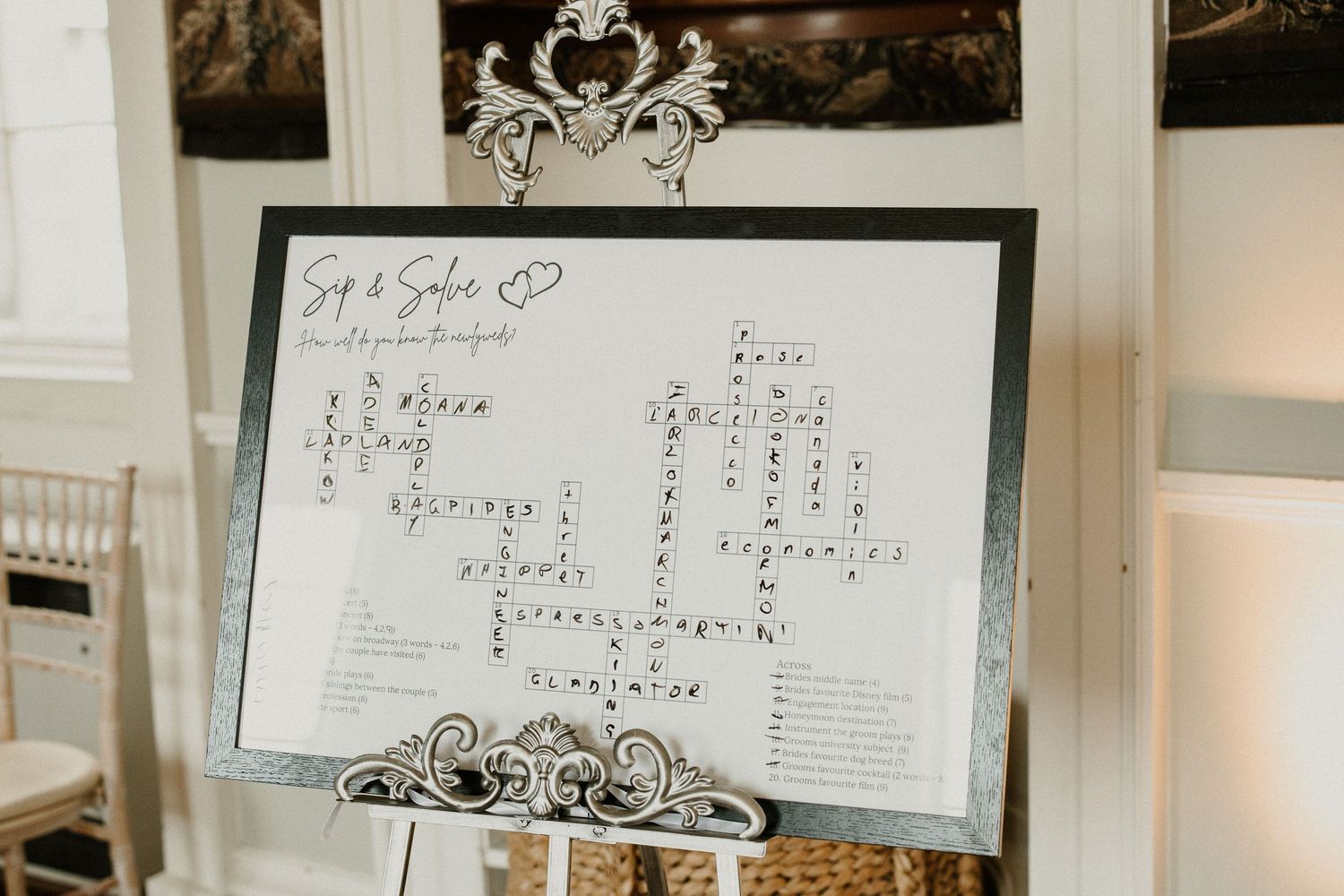Elegant wedding seating chart display with ornate silver frame and decorative details.