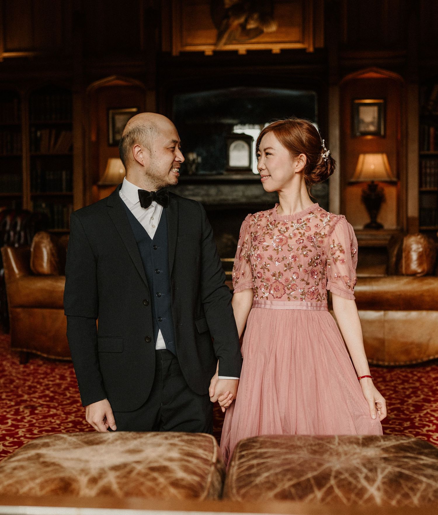 Couple in formal attire posing together in an elegant library setting.