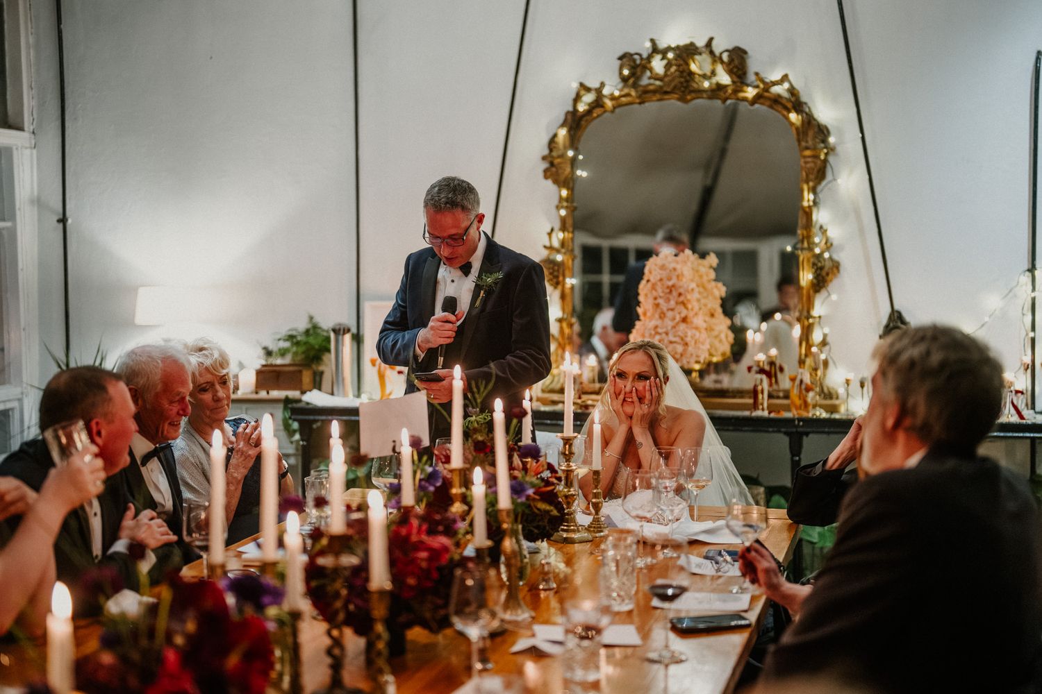 Elegant dining setup with ornate gold mirror, candlelight, and guests enjoying a celebratory evening.