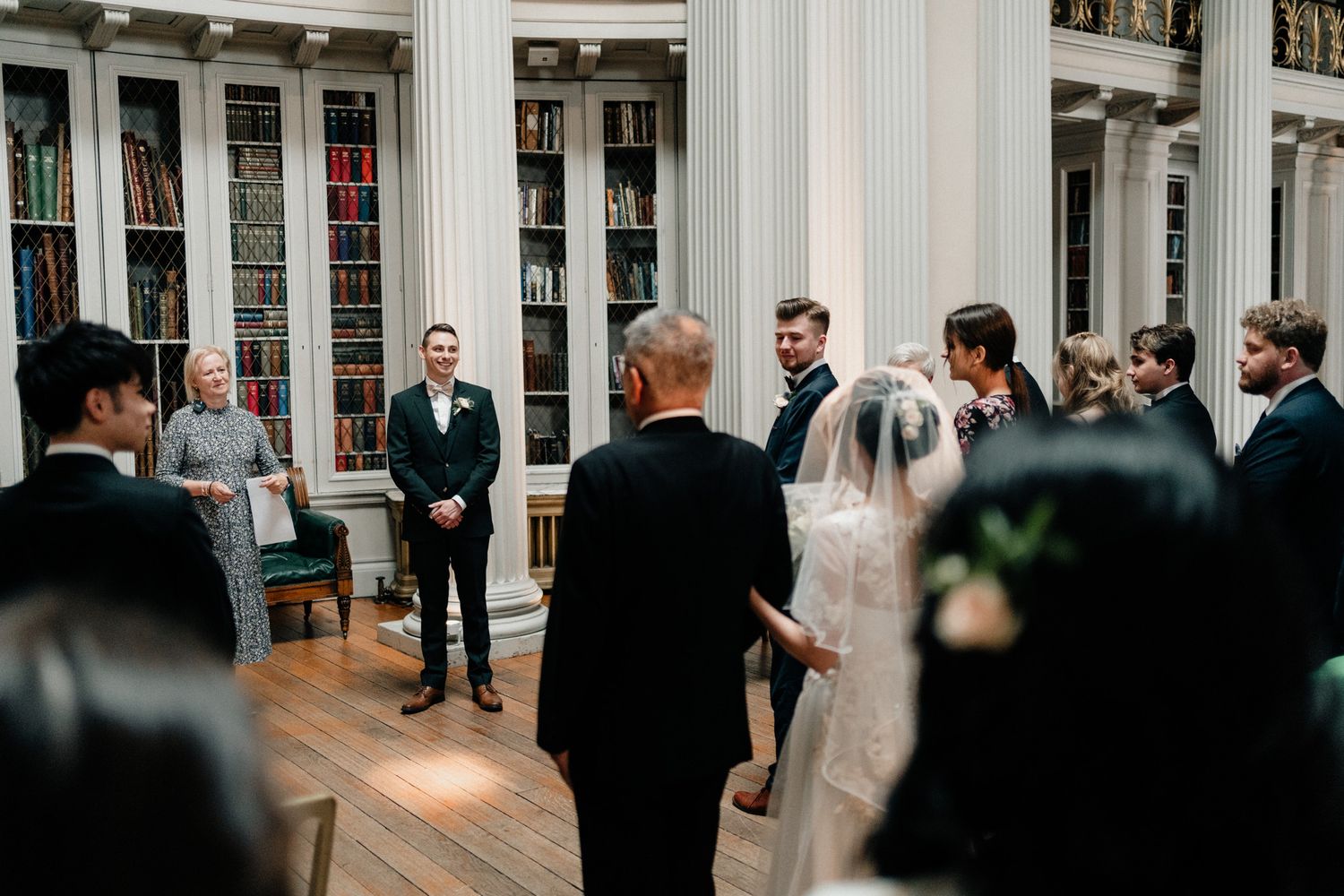 Wedding ceremony in progress in an elegant hall with white columns and high ceilings.