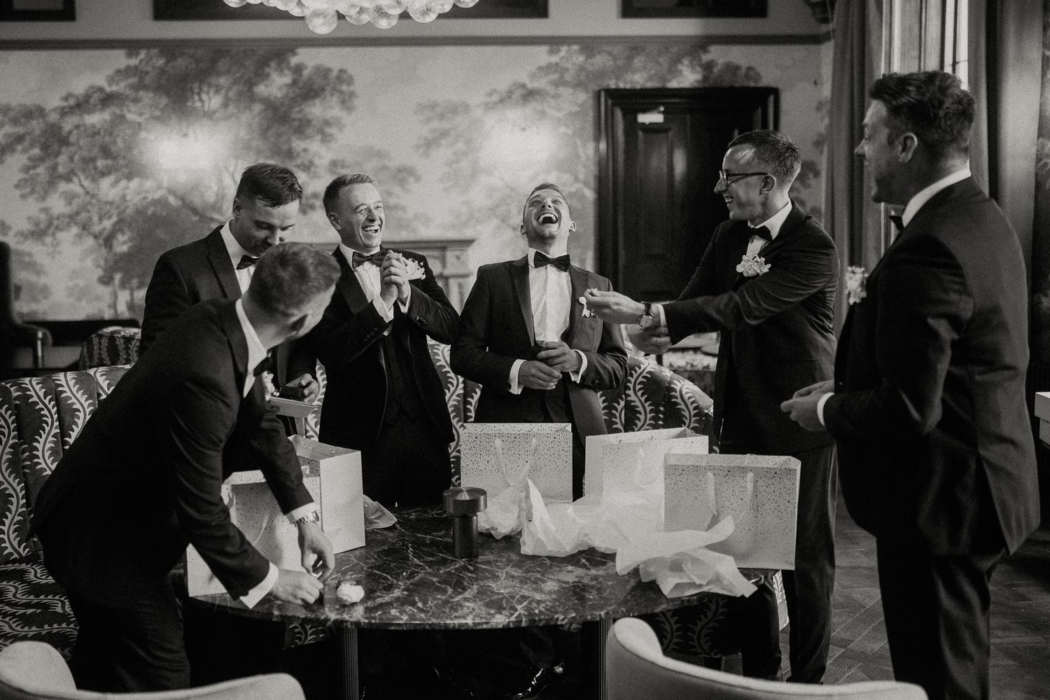 A vintage black and white photograph shows a group of men in tuxedos laughing together at a formal gathering.