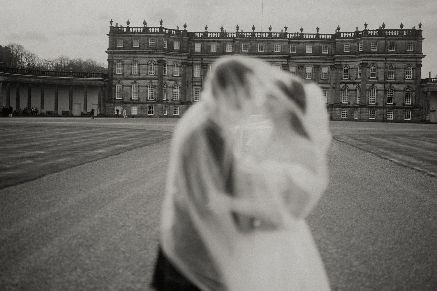 Elegant bridal veil flows in the wind with stately manor house in background.