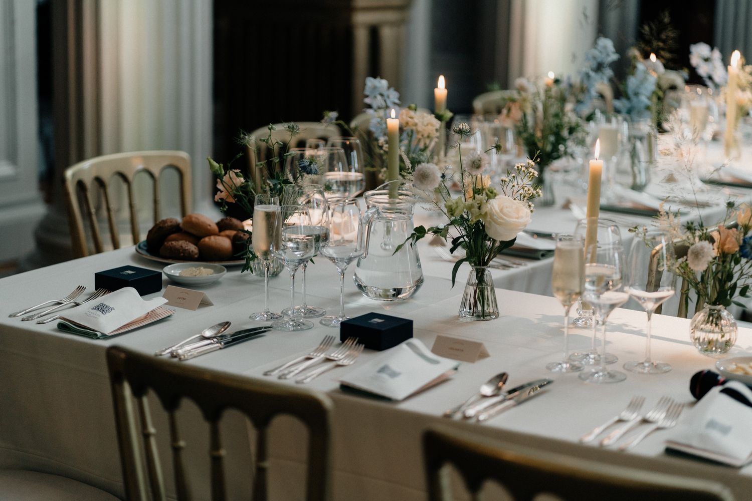 Elegant wedding reception tables set with white linens, floral centerpieces, and glowing candles in a formal dining space.