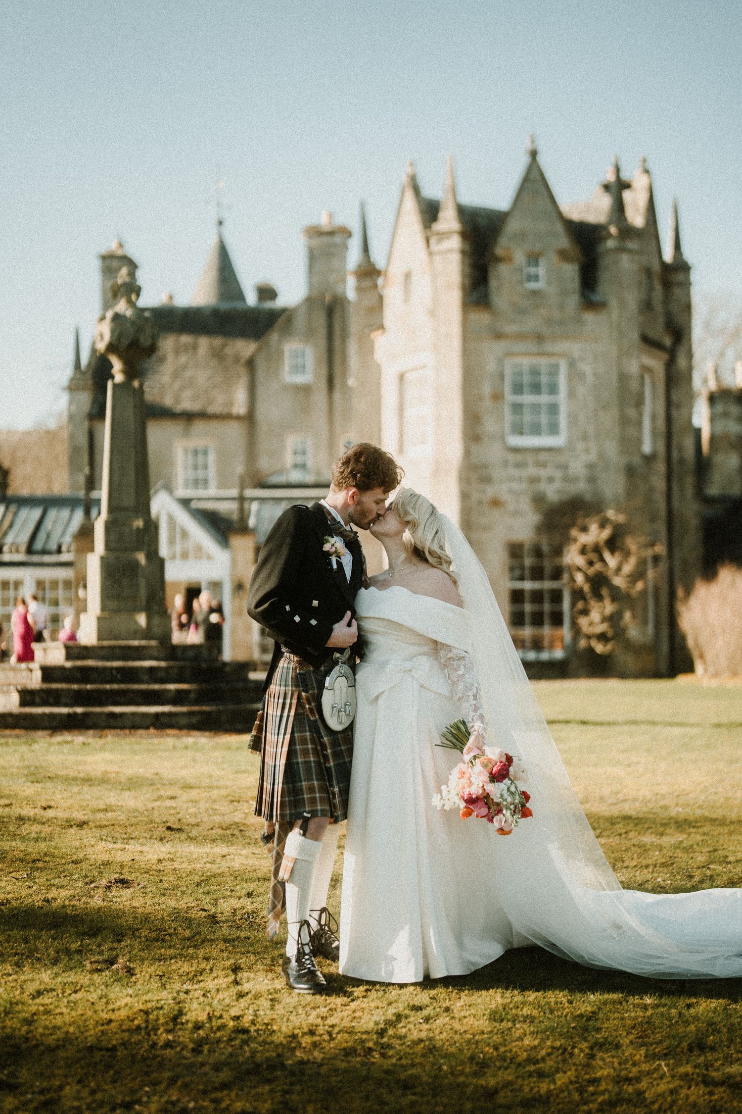 Romantic embrace between newlyweds in Scottish wedding attire against historic castle backdrop.