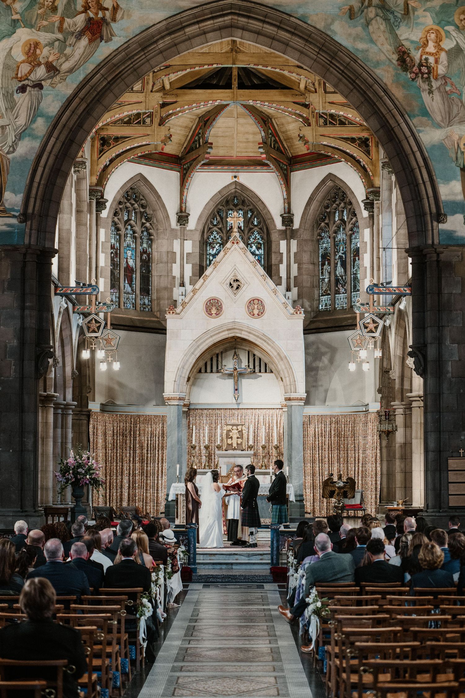 Stunning church interior with gothic architecture, stained glass windows and painted ceiling during ceremony.