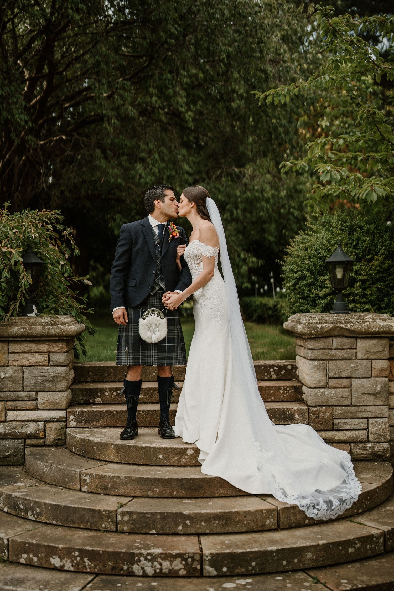 Couple shares romantic moment on stone steps in garden setting.