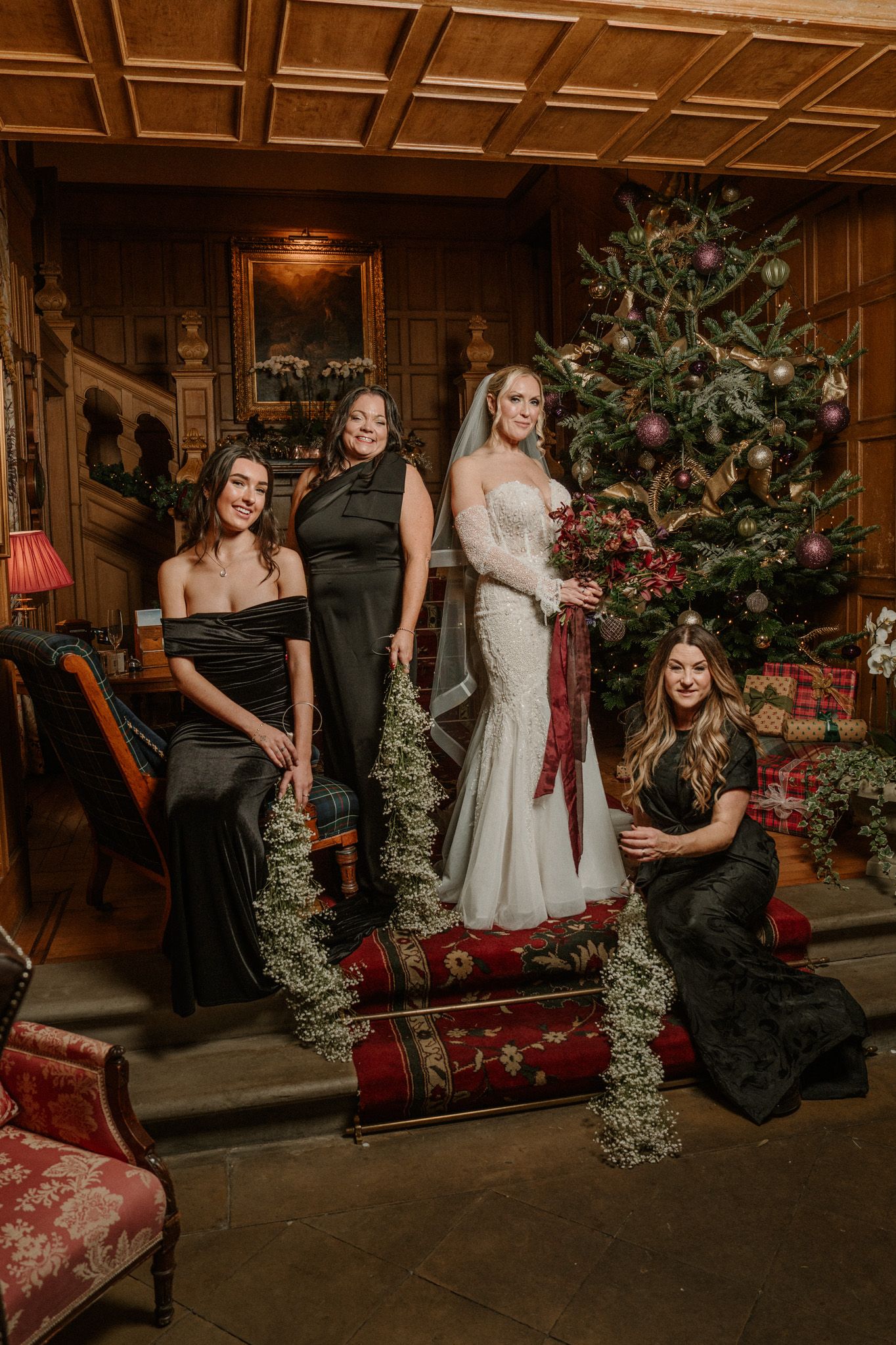 Wedding party poses informally on grand staircase with Christmas tree and holiday decorations.