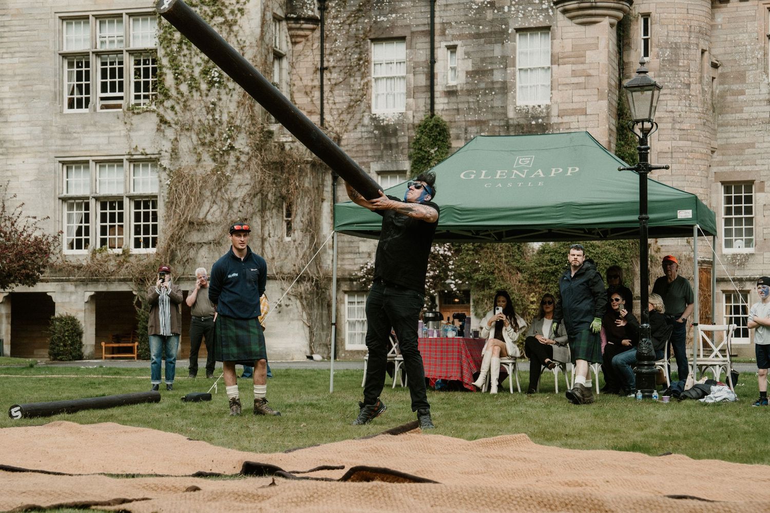 People participate in an outdoor axe-throwing event near a historic stone building.