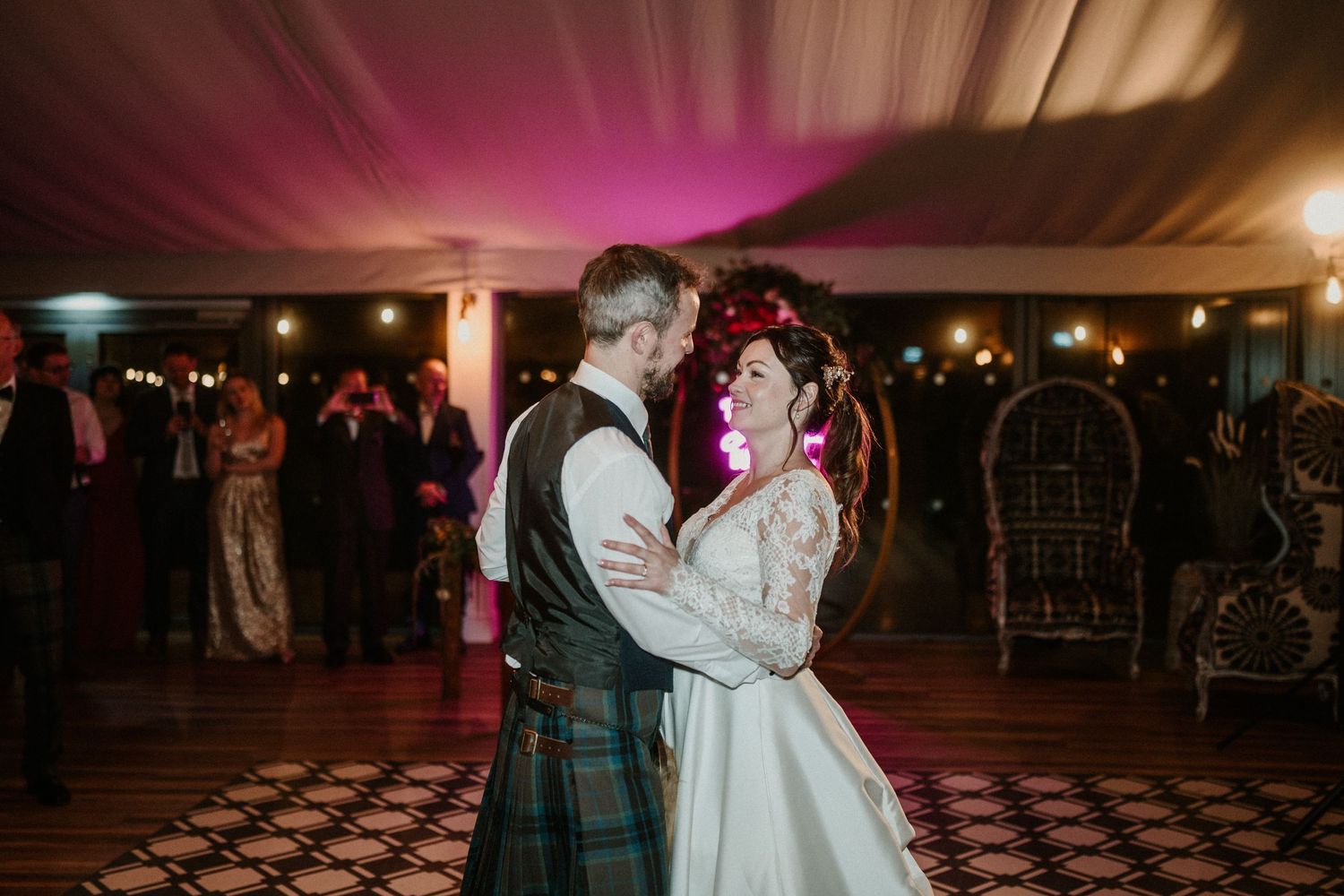 A romantic dance between newlyweds, with the groom in traditional Scottish kilt at an indoor reception.