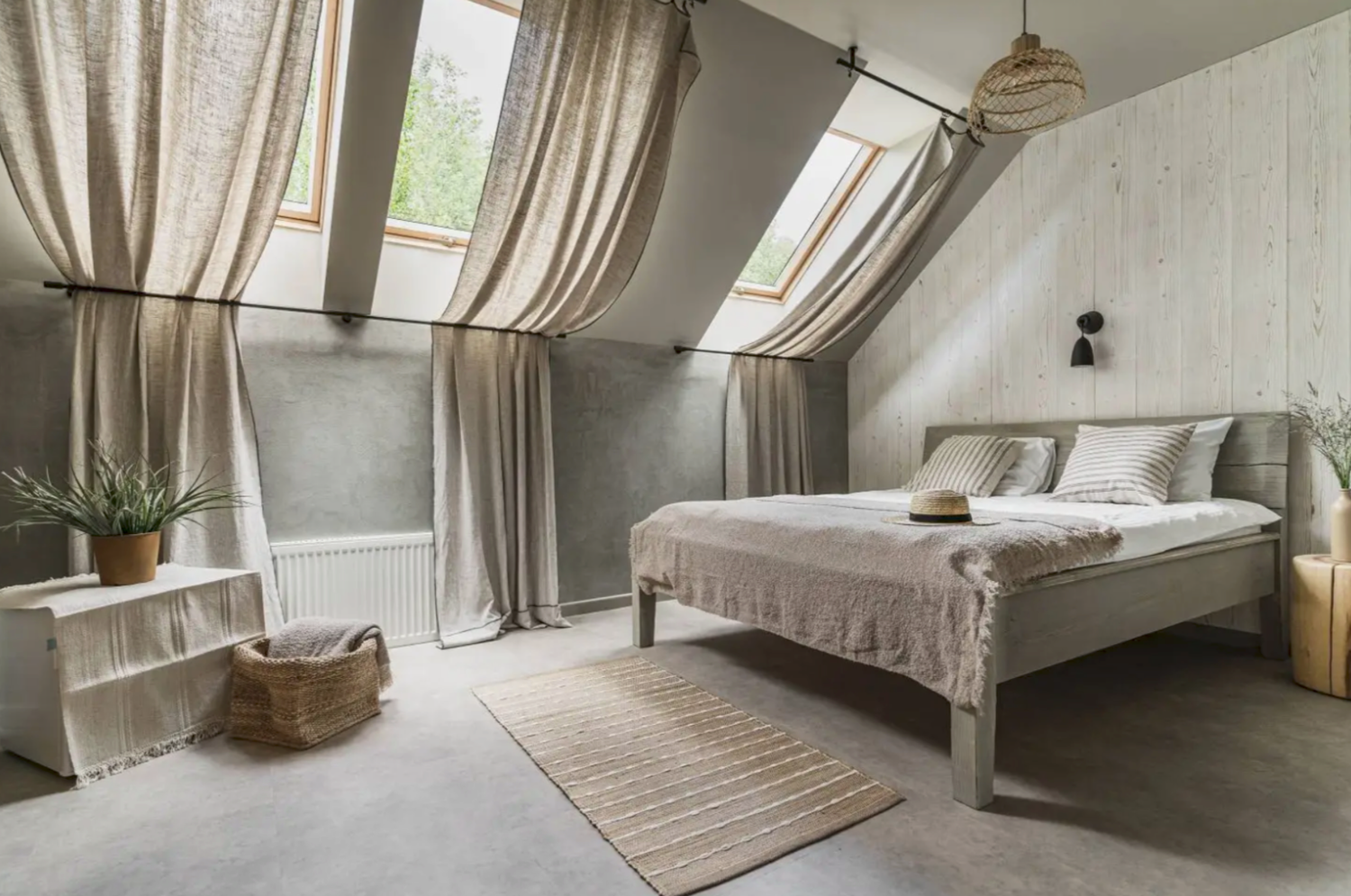 Cozy attic bedroom with linen curtains, skylight windows, a neutral-toned bed, and rustic woven decor accents.