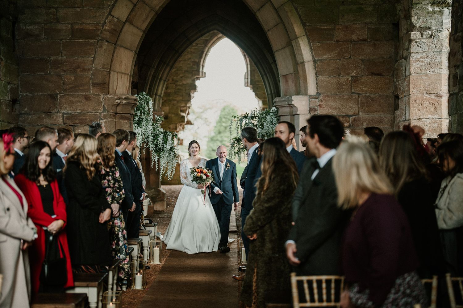 Wedding ceremony in a rustic stone church with guests seated in wooden chairs and floral decorations.