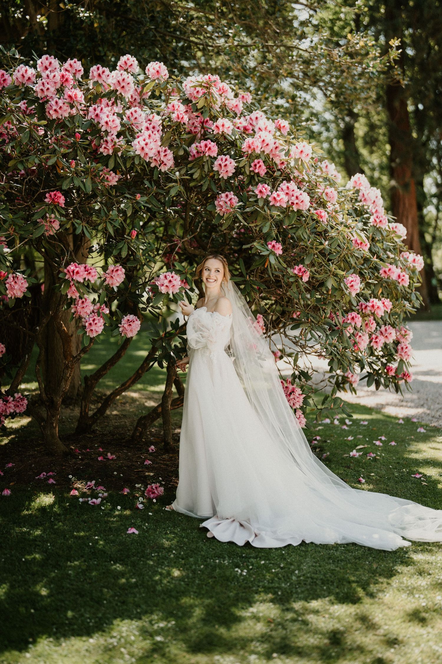 Elegant white wedding gown photographed against blooming pink flowers in a garden setting.