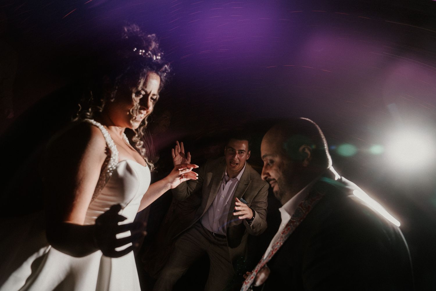 Silhouettes of wedding guests dancing in a dimly lit reception space with dramatic spotlights.