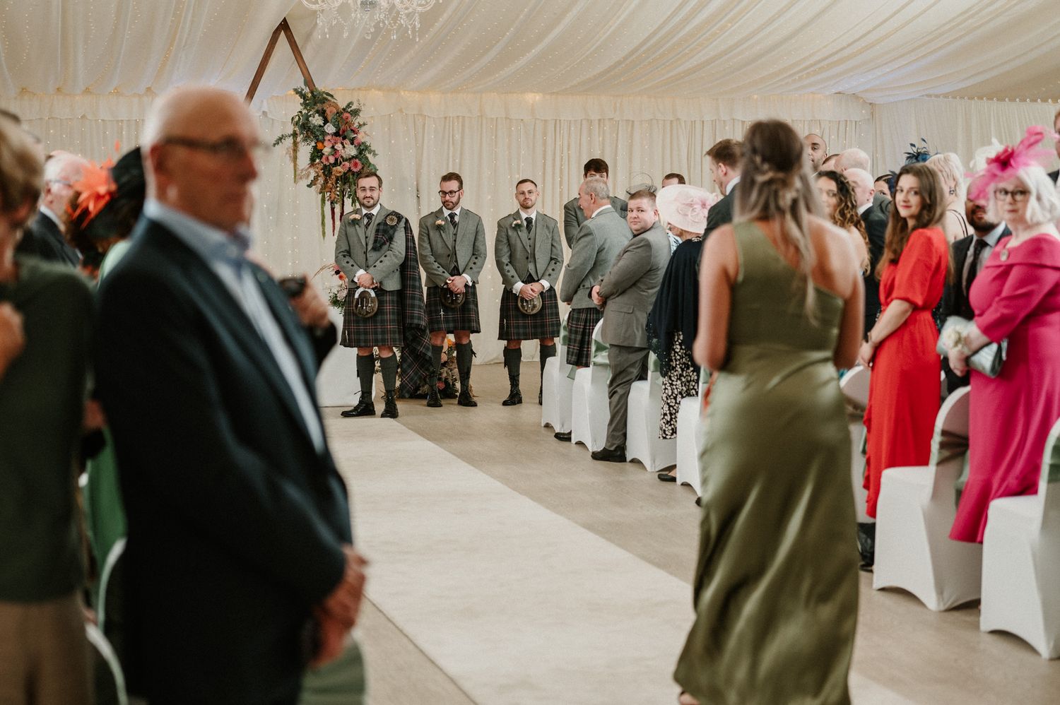 Wedding reception venue decorated with elegant white draping and chandeliers showing guests mingling.