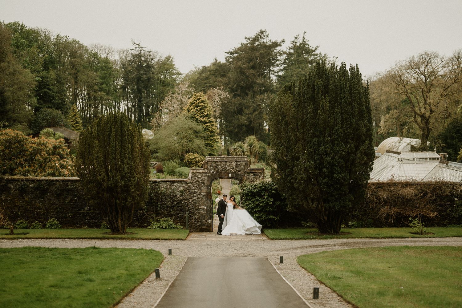 A distant view of a wedding couple framed by cypress trees in a formal garden setting.