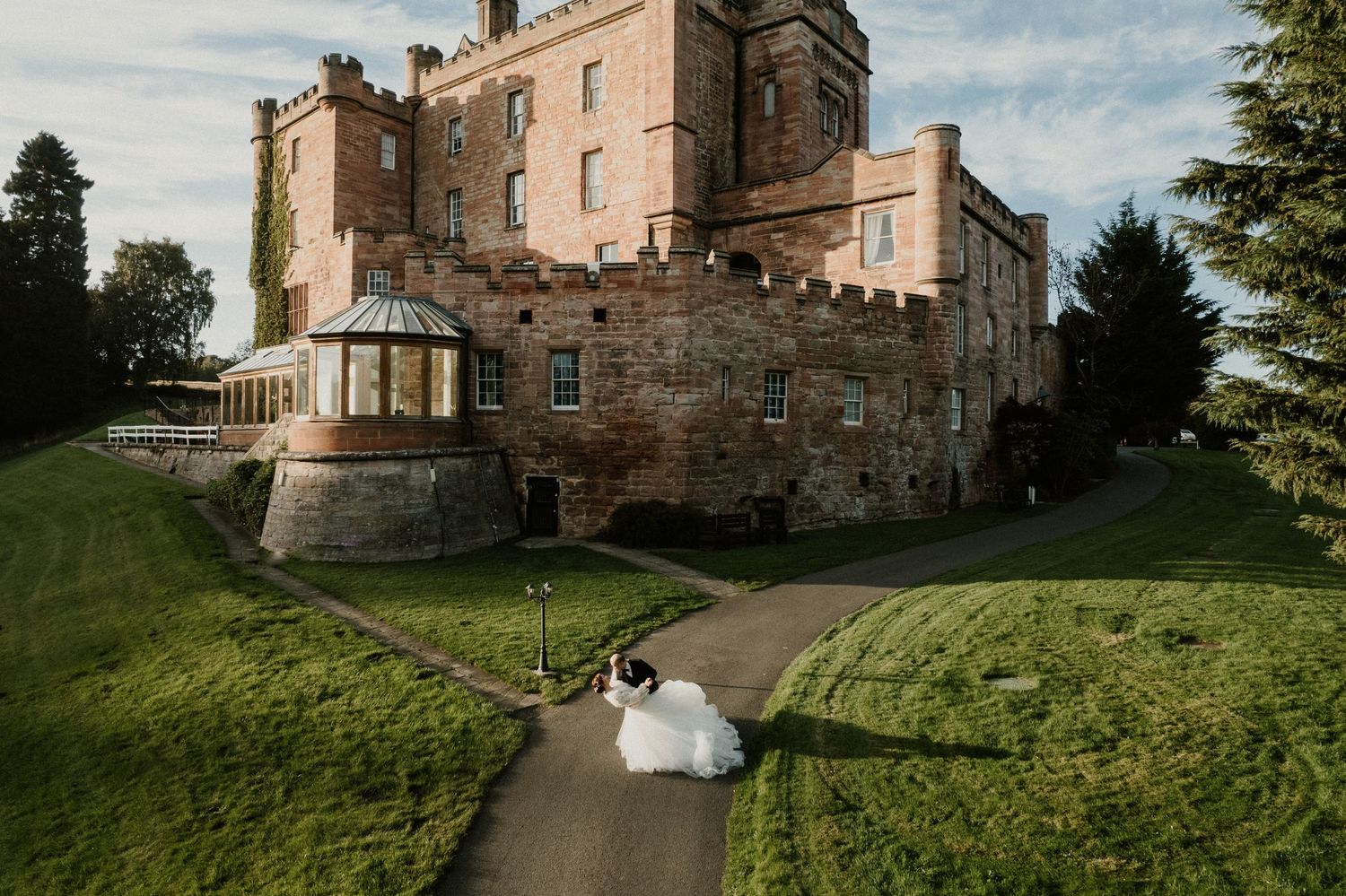 A grand stone castle with turrets and towers sits majestically on a green hillside under blue skies.
