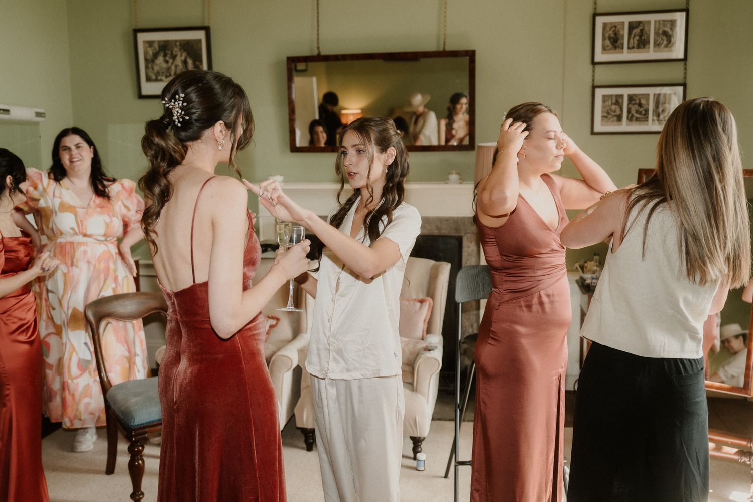 Bridesmaids in red and rose gowns getting ready together in an elegant room before a wedding ceremony.