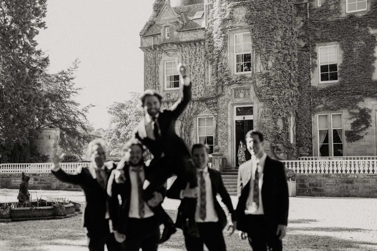 Groomsmen and wedding party jumping for joy in black and white photo outside historic building.