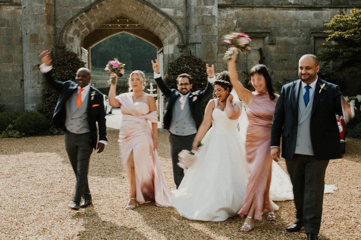 Wedding party poses playfully outside historic stone castle entrance.