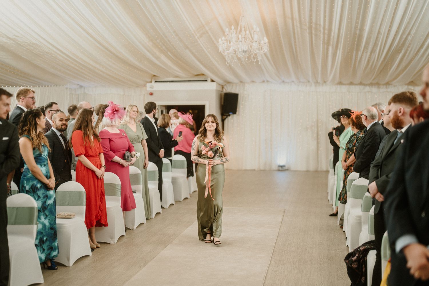 Wedding guests seated in rows at an elegant indoor reception with draped white fabric ceiling.