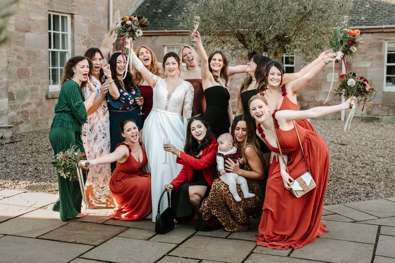 Wedding party group sitting on stone steps outside a historic building.