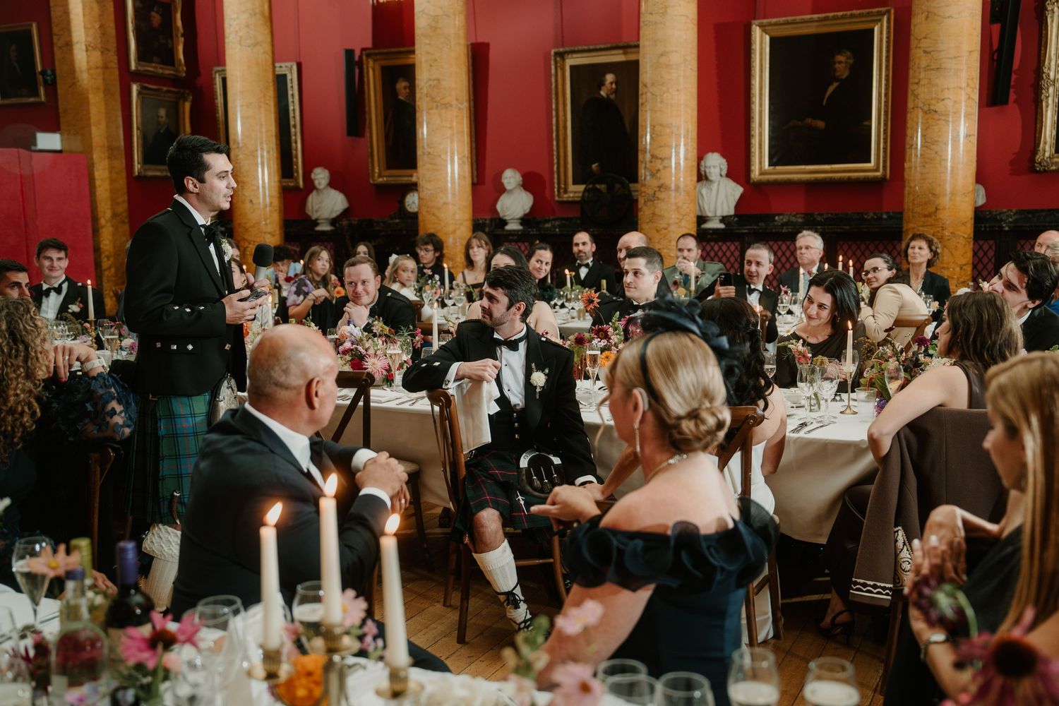 Wedding celebration in an opulent red dining hall with guests raising glasses in a toast.