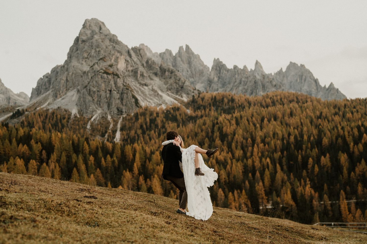 Elegant white dress contrasts against rugged mountain landscape and golden forest.