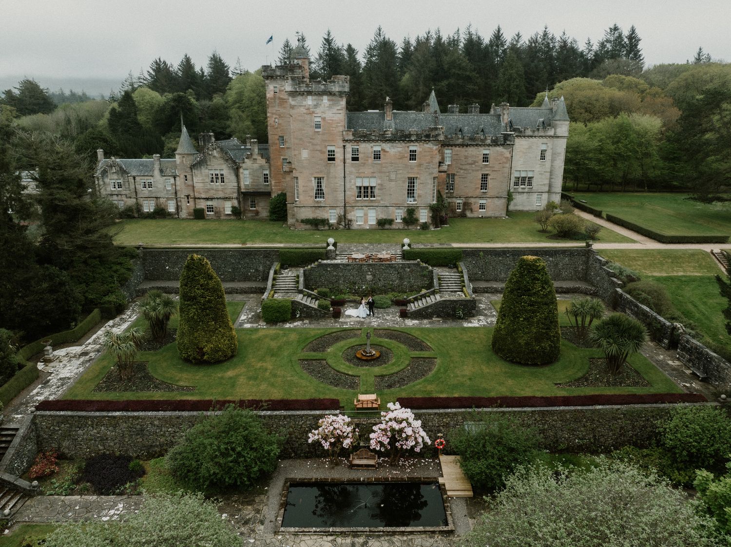 Aerial view of a grand Scottish castle estate with manicured gardens and surrounding countryside.