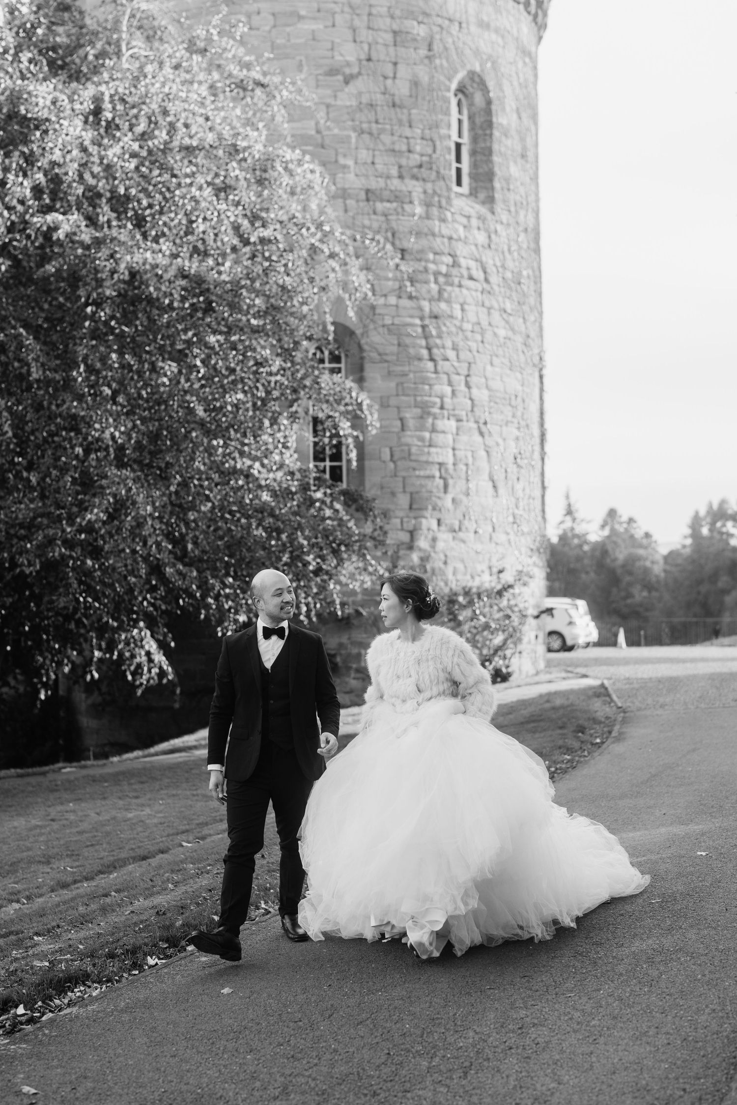 A black and white photo of a couple dancing near a stone tower.