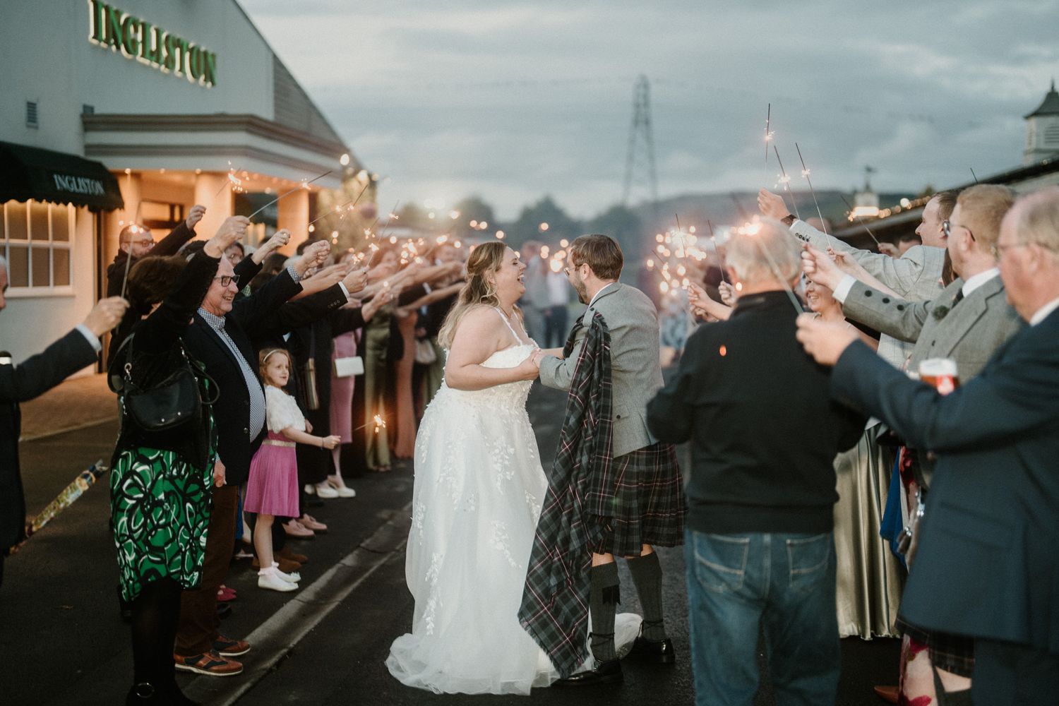 Wedding party exits while guests throw confetti under moody skies.