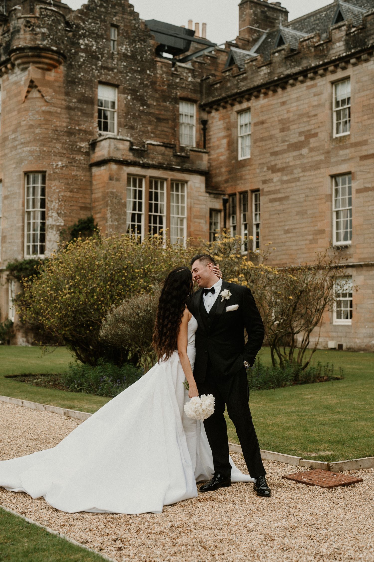 A tender wedding moment captured in front of a beautiful stone castle with manicured grounds.