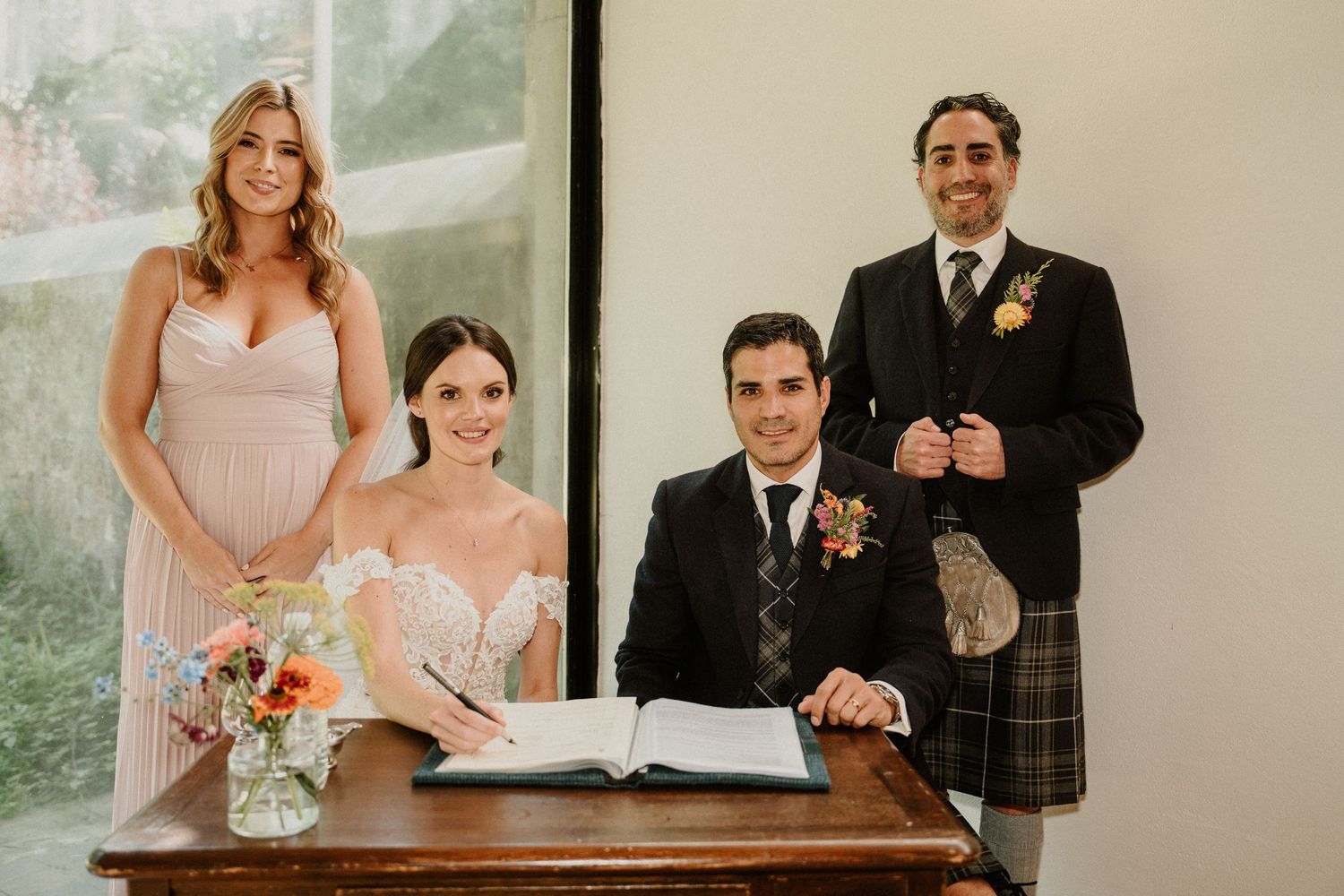 Wedding party signing documents at a wooden table during the ceremony.