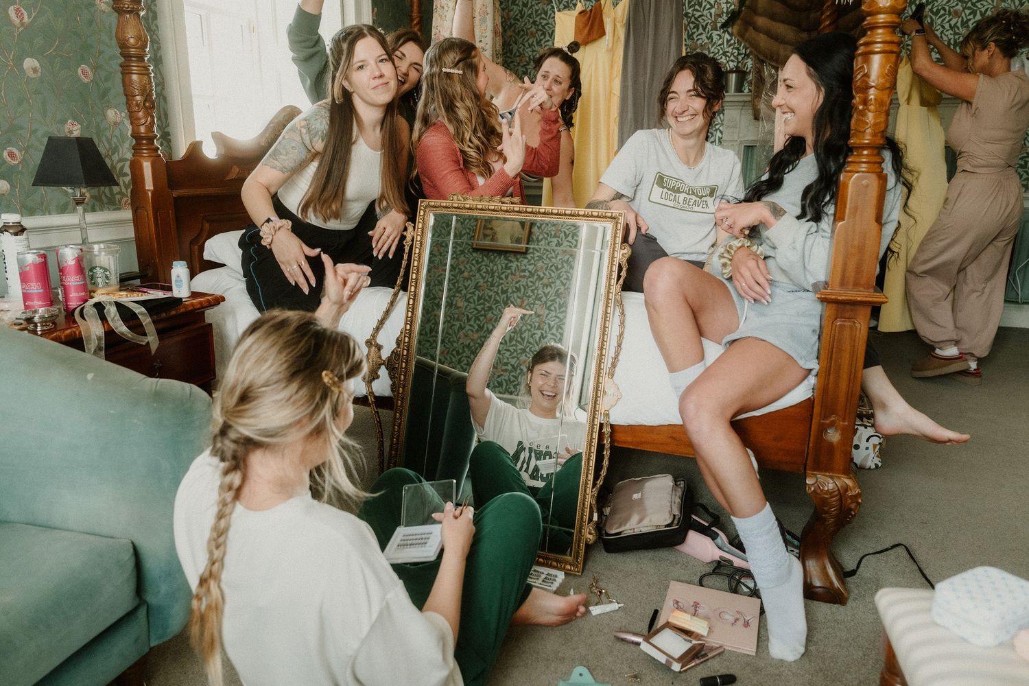 Group of bridesmaids laughing and celebrating in a decorated bedroom during wedding preparations.