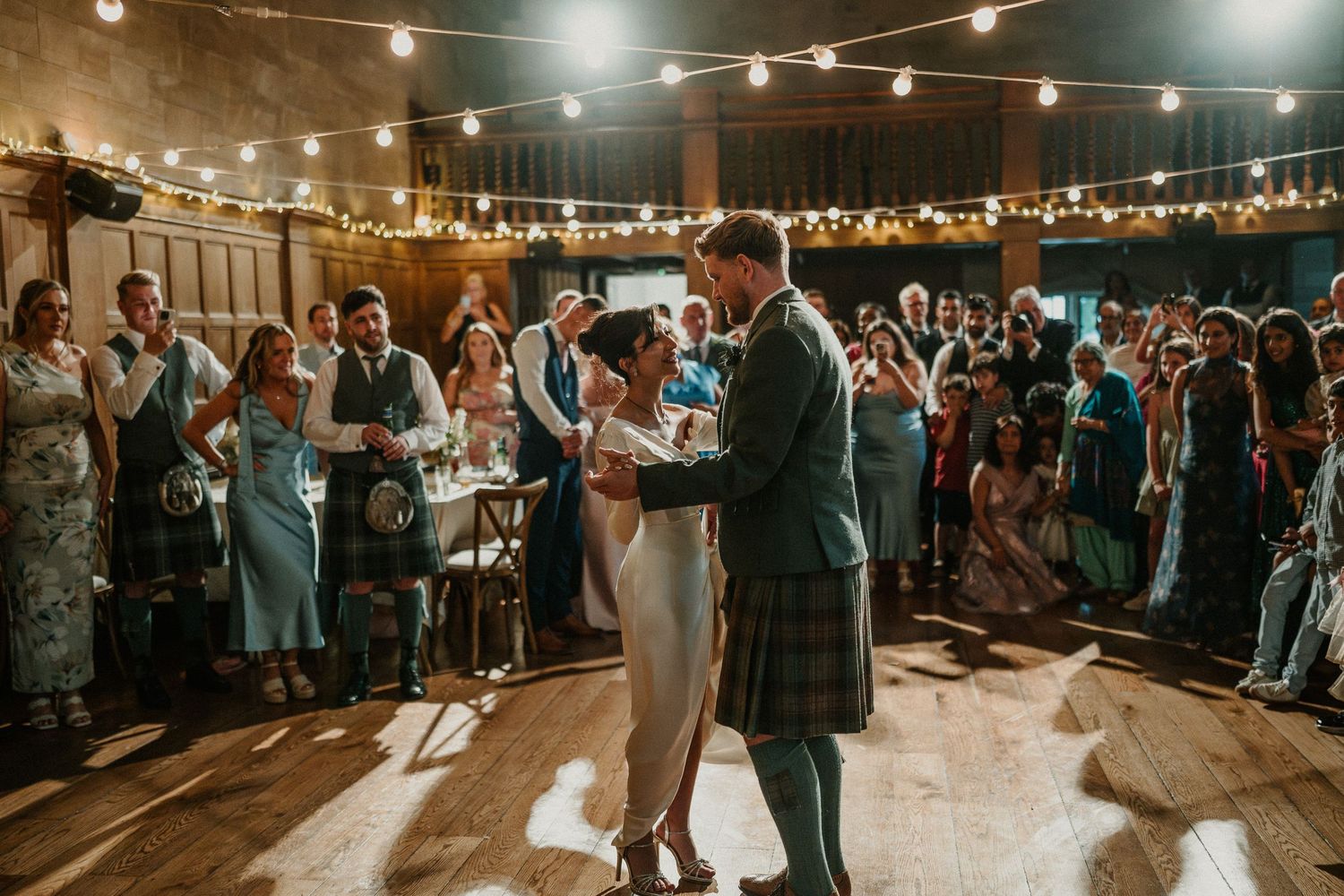Wedding guests dancing and celebrating on a dimly lit dance floor under string lights.