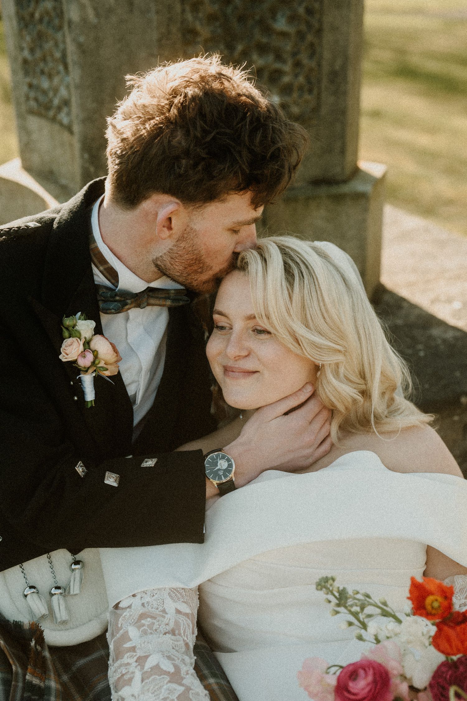 Intimate moment between newlyweds in Scottish wedding attire during an outdoor ceremony.